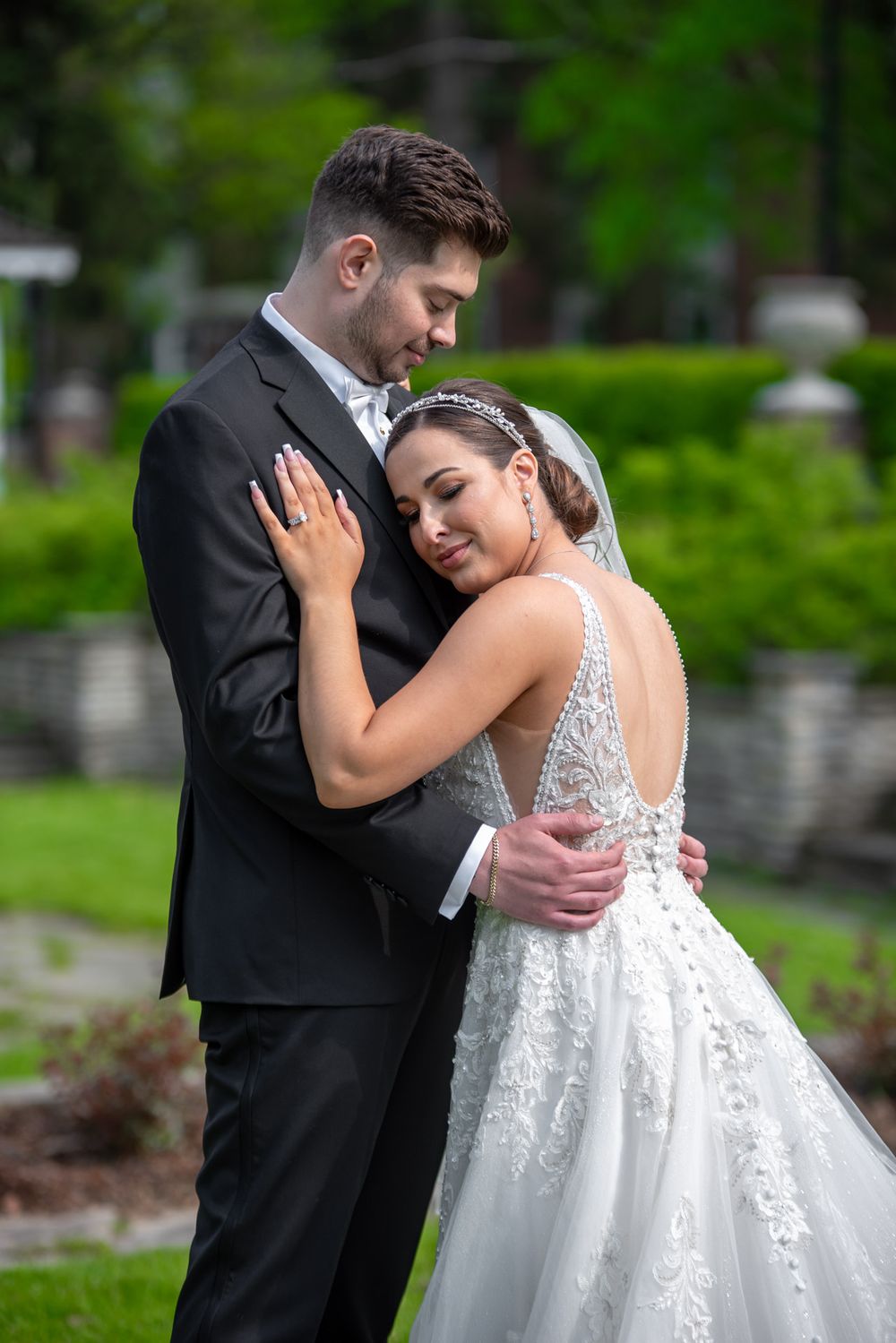 Bride rests her head on grooms chest as they share an intimate embrace in a garden.