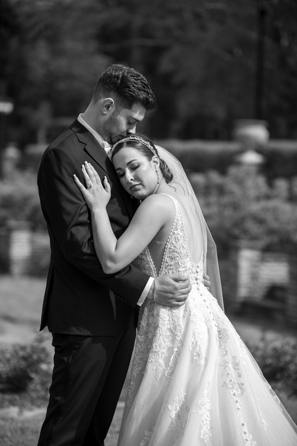 Black and white portrait of bride leaning into grooms chest in a tender garden embrace.