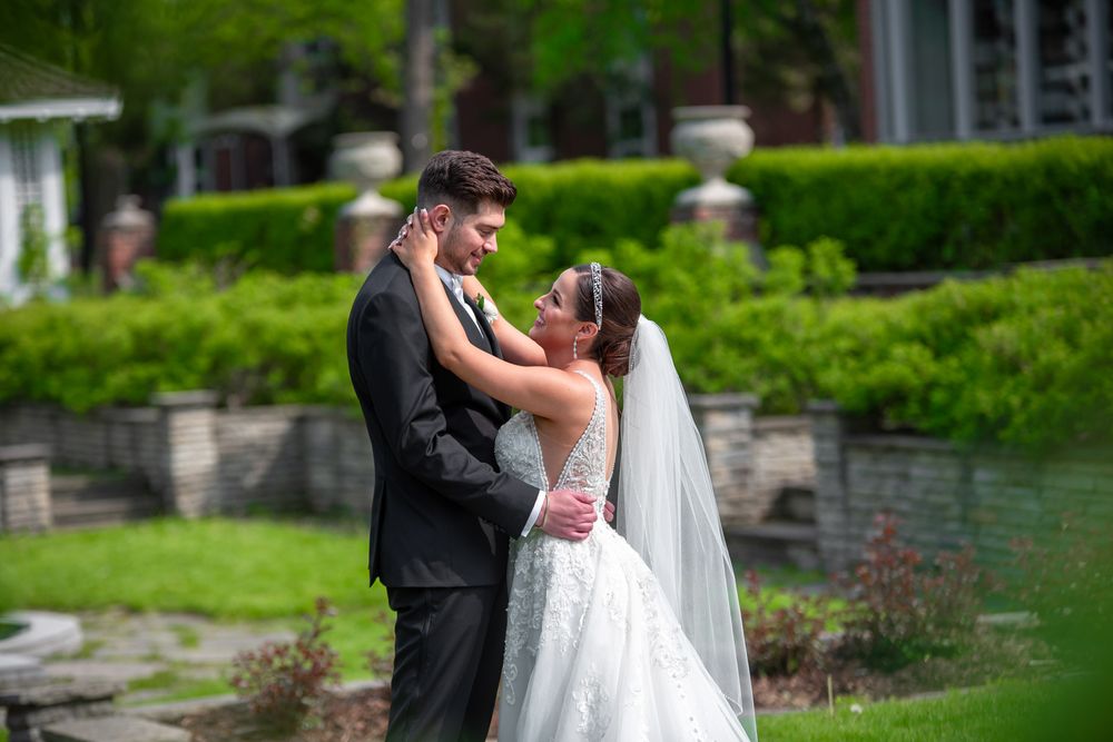 Bride and groom gazing at each other lovingly in a lush green garden with stone wall backdrop.
