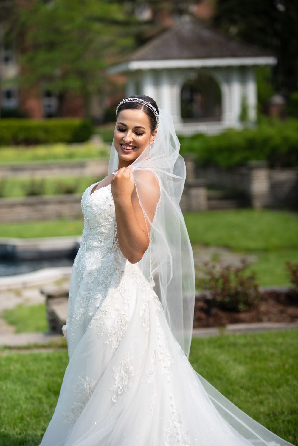 Joyful bride twirling her veil in a lace wedding dress in a sunny garden.