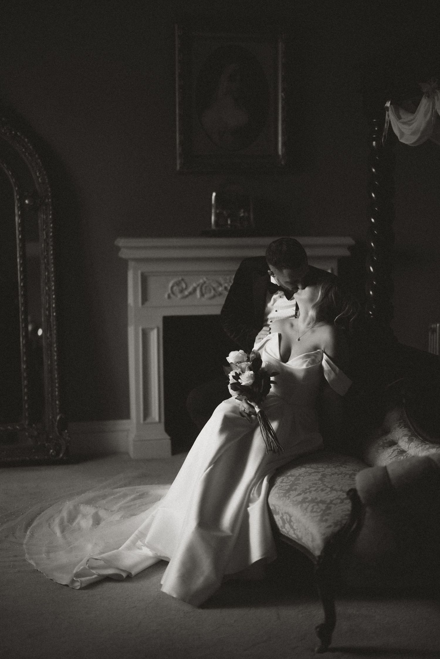 A black and white image of a wedding couple kissing whilst the bride holds a bouquet of flowers.