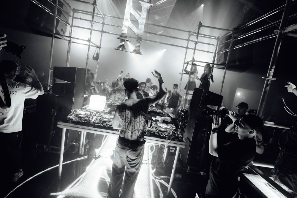 Black and white nightclub scene with dramatic lighting and audio equipment in the background.