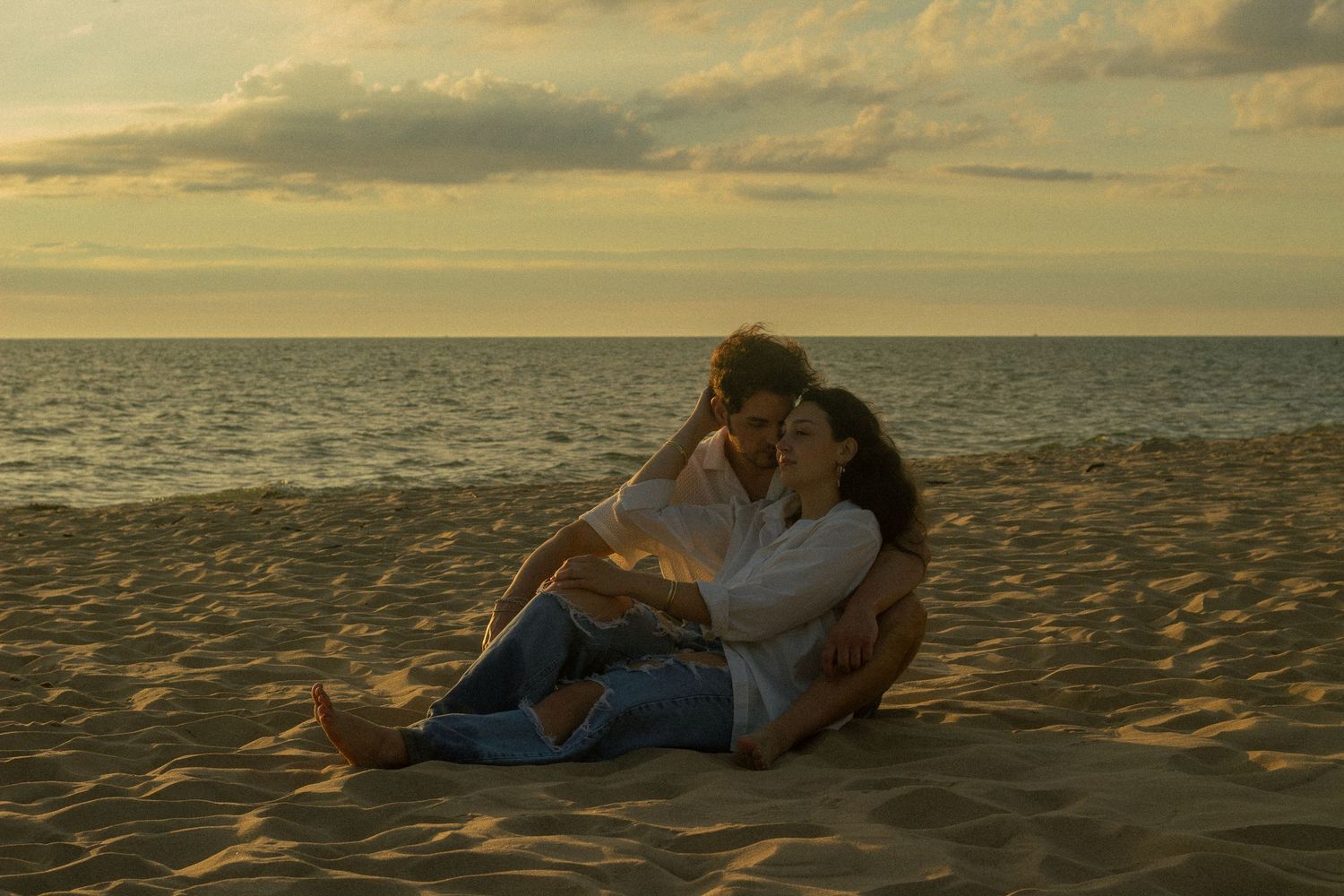 A couple embraces as they lay on the beach for couples photos in Saugatuck, Michigan.
