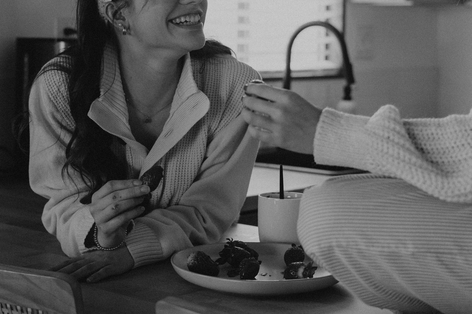A person wearing a striped shirt smiles while relaxing at home with a plate of food.
