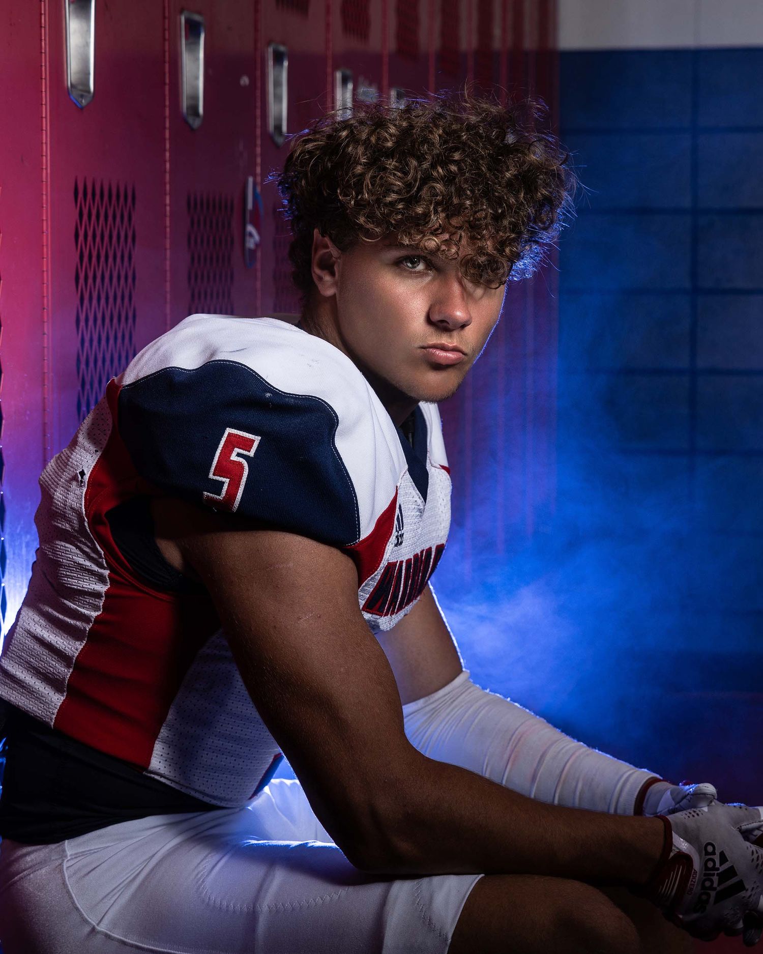 Football player in jersey number 5 poses in locker room with dramatic lighting.