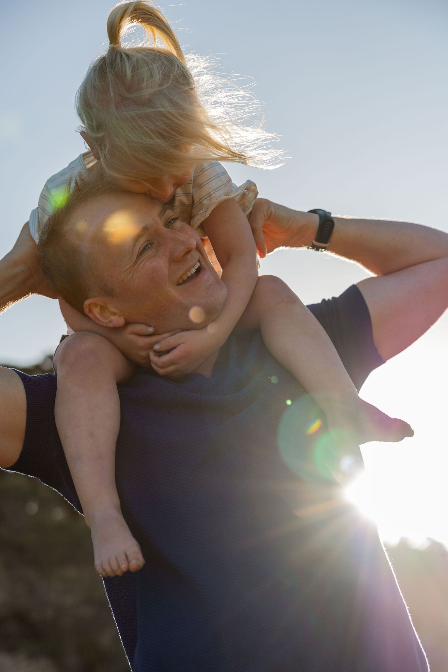 A dad lifting his young daughter high into the air, both laughing with joy as the sun sets behind them in a golden glow.