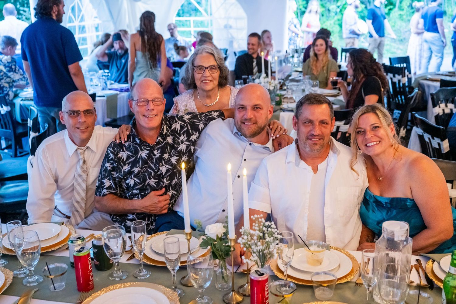 Group of six smiling guests posing together at an elegant candlelit wedding reception dinner table.