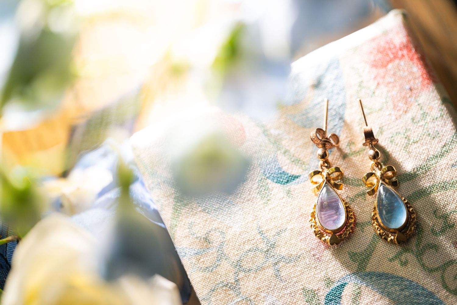 Elegant gold drop earrings with blue and lavender gemstones displayed on floral fabric.