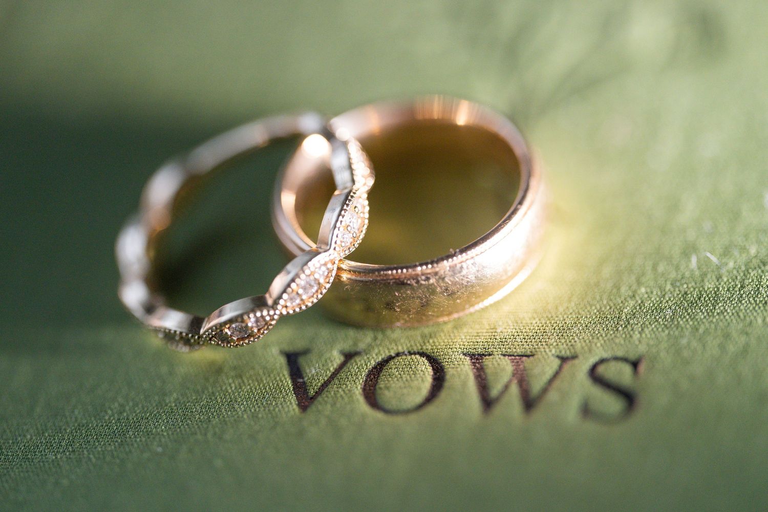 Two gold wedding rings resting on a green book open to a page that reads Vows.