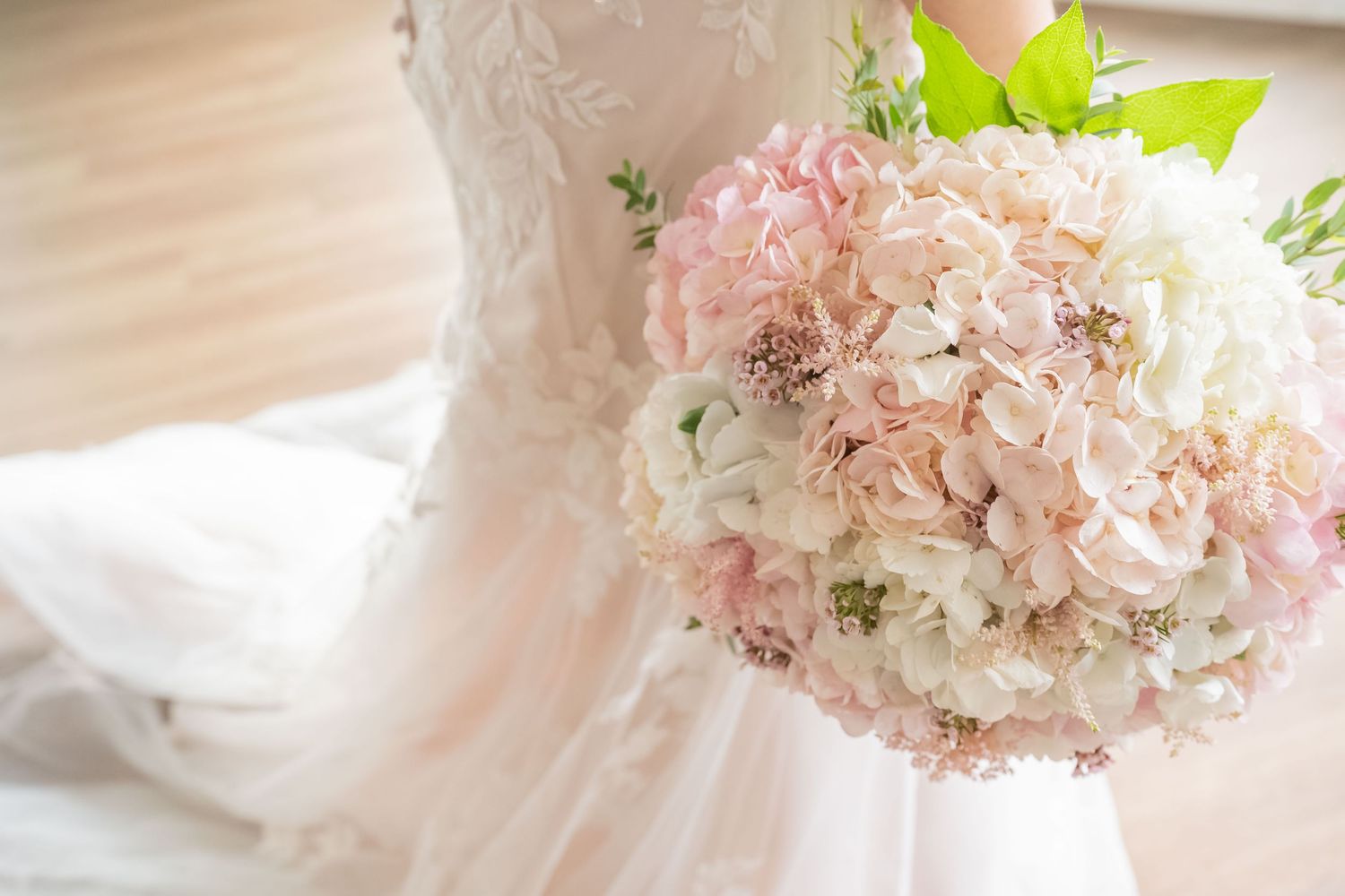 Bride holding a lush pink and white hydrangea wedding bouquet in front of her white lace gown.