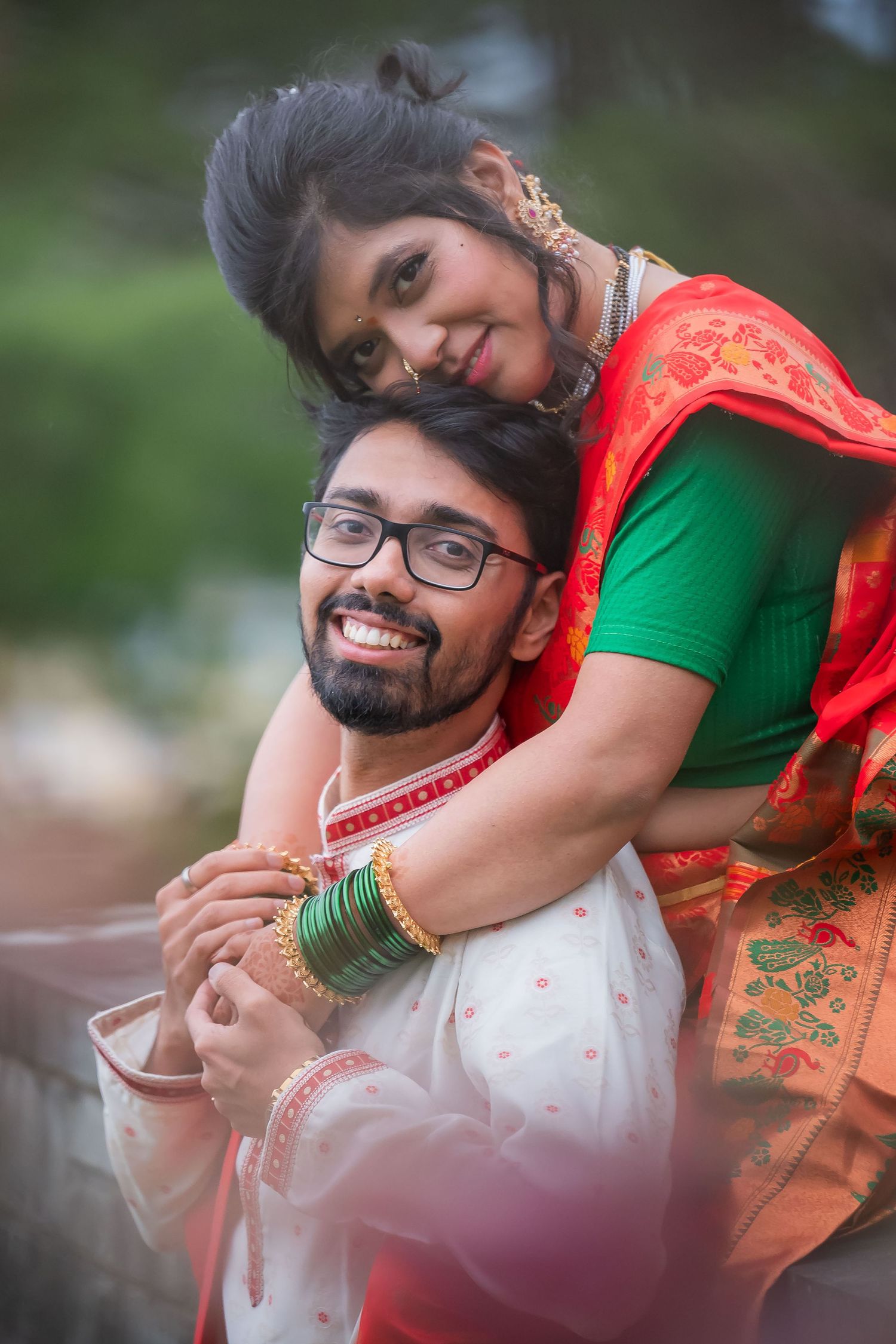 Joyful Indian couple in traditional wedding attire sharing a romantic piggyback pose outdoors.