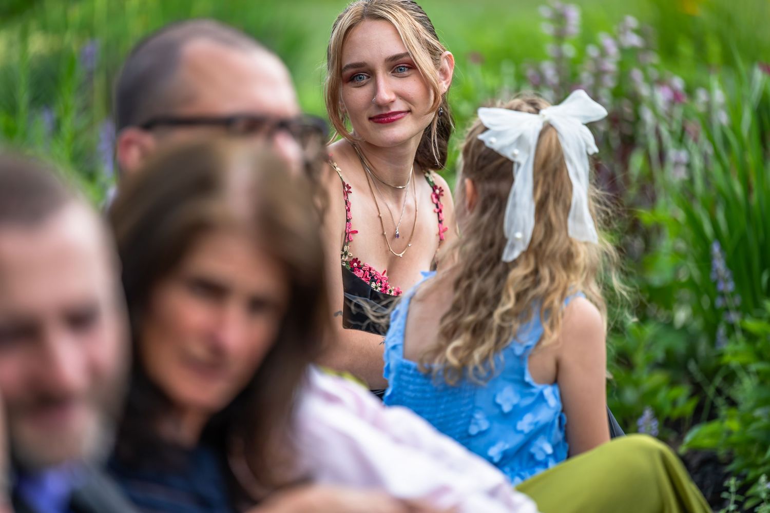 Young woman in floral dress smiling at child during outdoor garden wedding celebration.