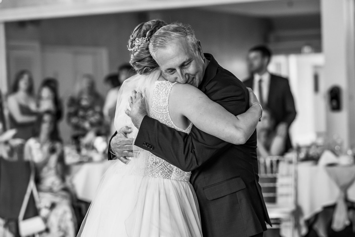 Bride and father share an emotional first dance hug at elegant wedding reception in black and white photo.