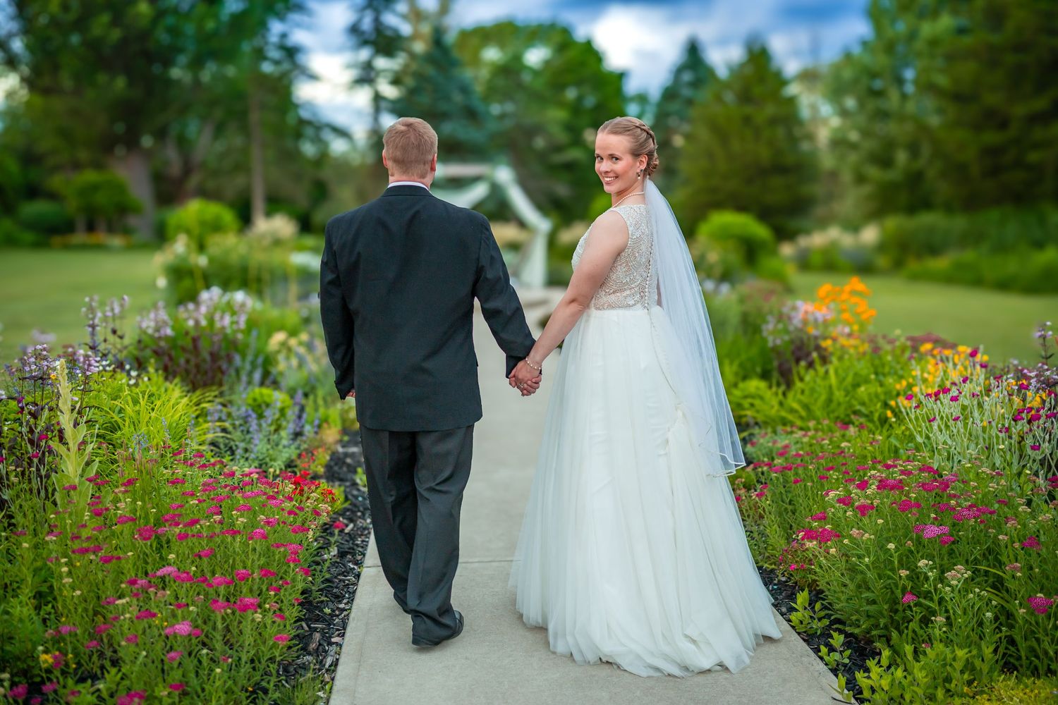 Bride and groom holding hands walking through vibrant flower garden on their wedding day.