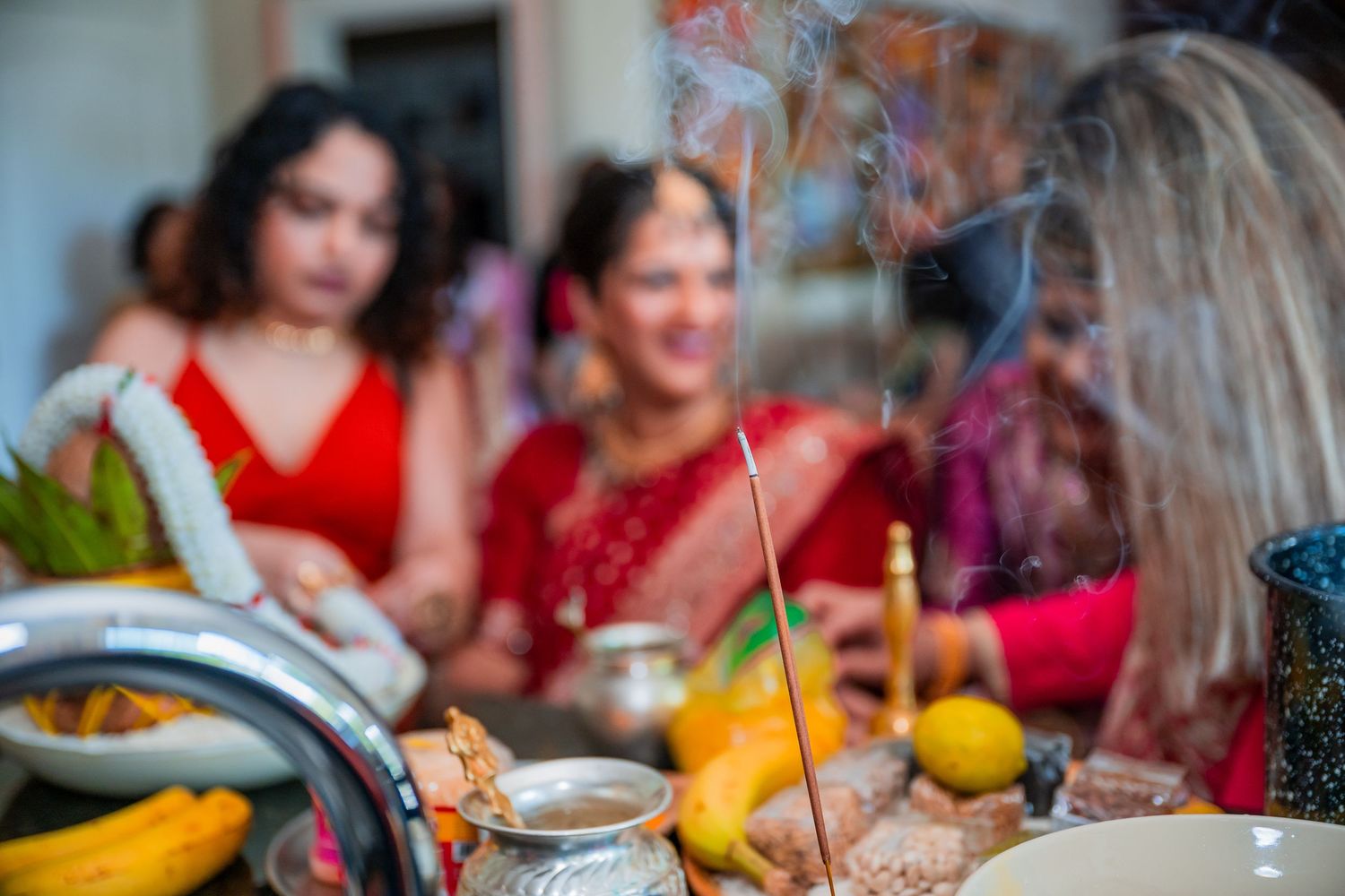 Women in red traditional Indian attire gathered around incense and offerings during a Hindu wedding ceremony.