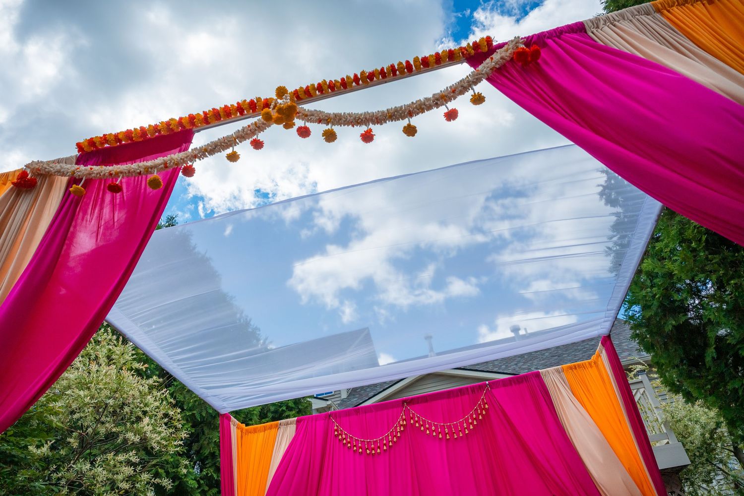 Colorful pink and orange mandap canopy with marigold garlands against blue sky at Indian wedding.