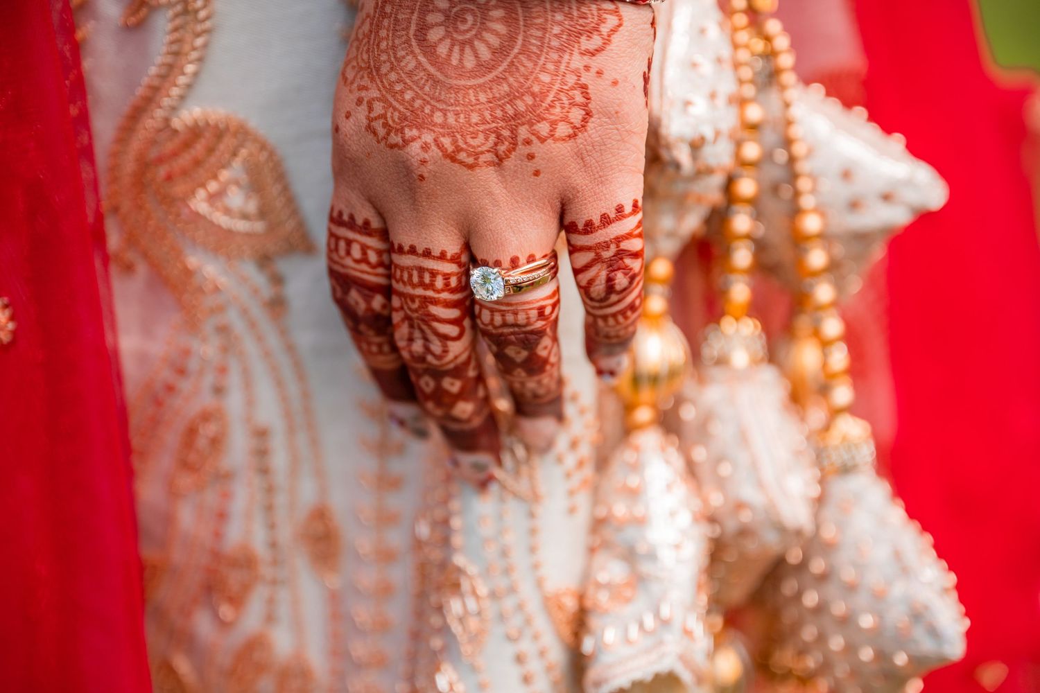 Close-up of a bride's hand adorned with intricate red henna mehndi design and gold rings at an Indian wedding.