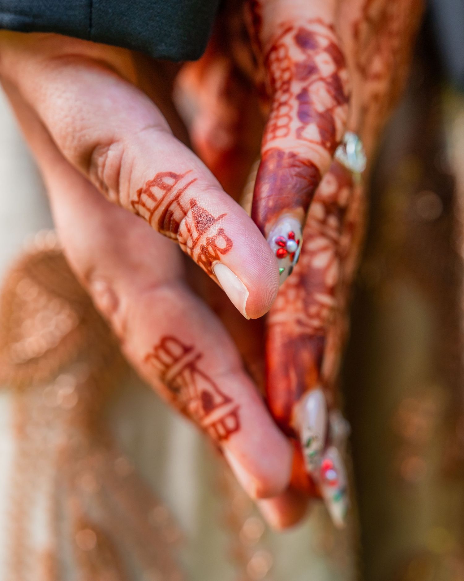 Close-up of hands adorned with intricate henna mehndi designs, featuring long decorated nails at a traditional wedding.