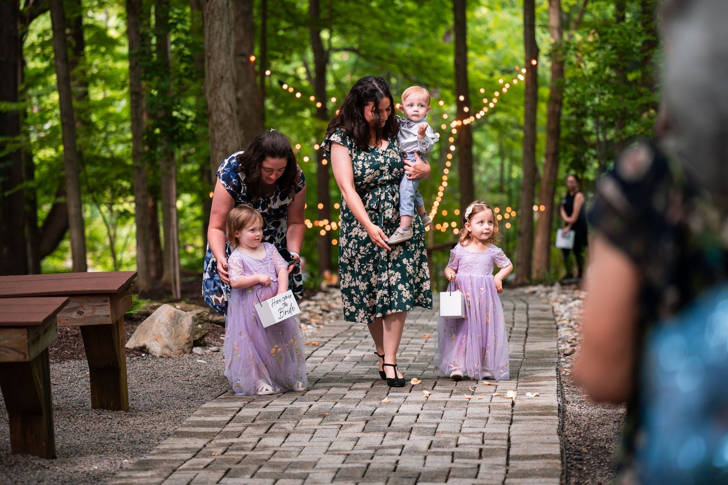 Flower girls in lavender tutus walking down stone path at outdoor woodland wedding ceremony.
