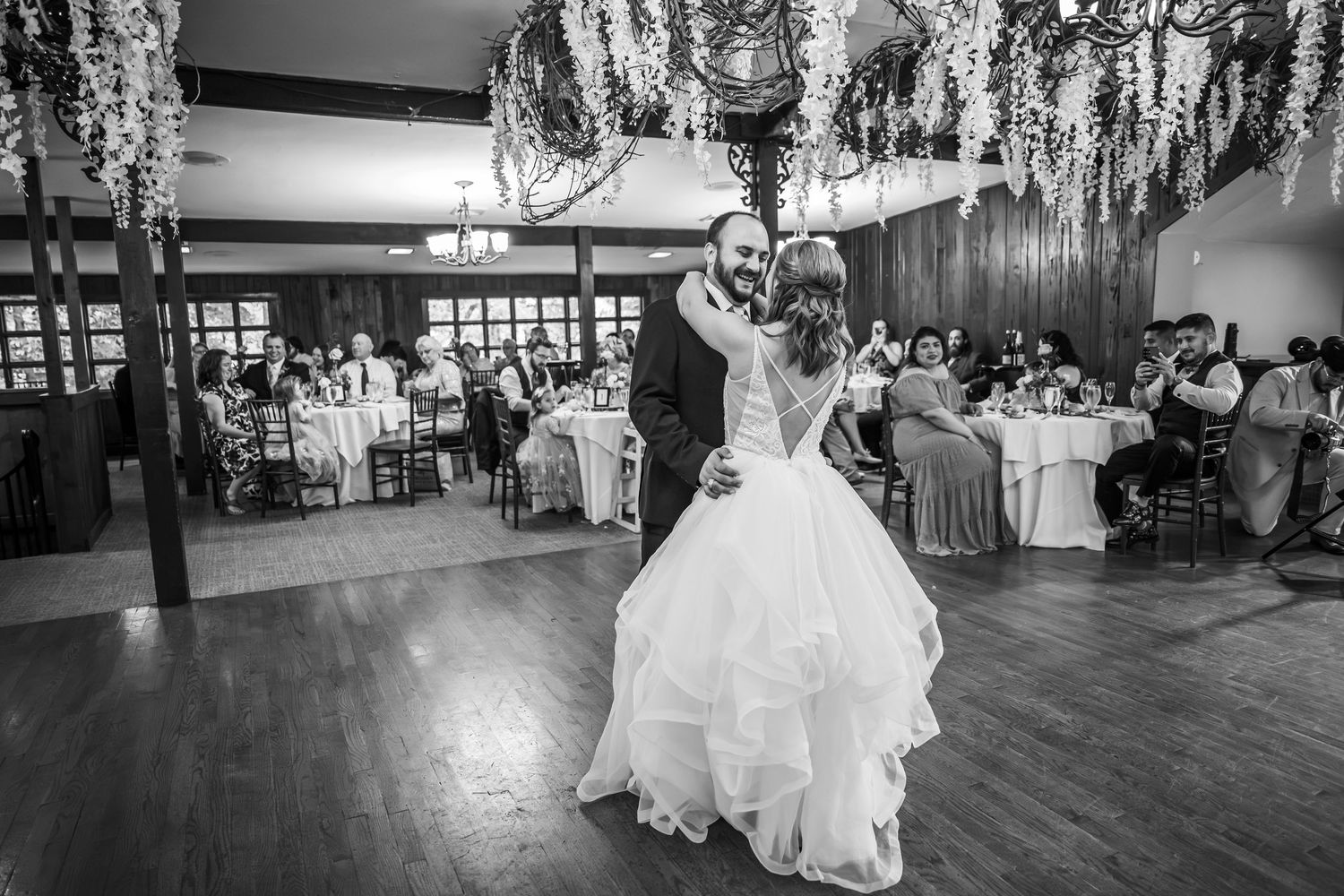 Black and white photo of a bride and groom sharing their first dance in a decorated wedding reception hall.