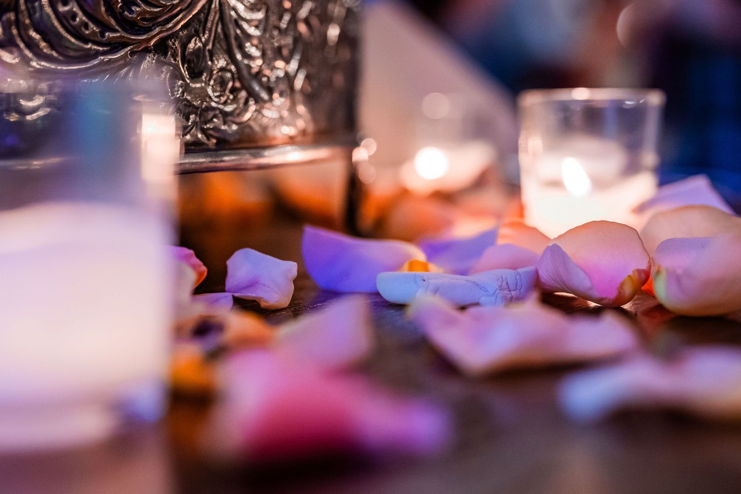 Scattered rose petals and glowing candles creating romantic wedding table centerpiece decor.