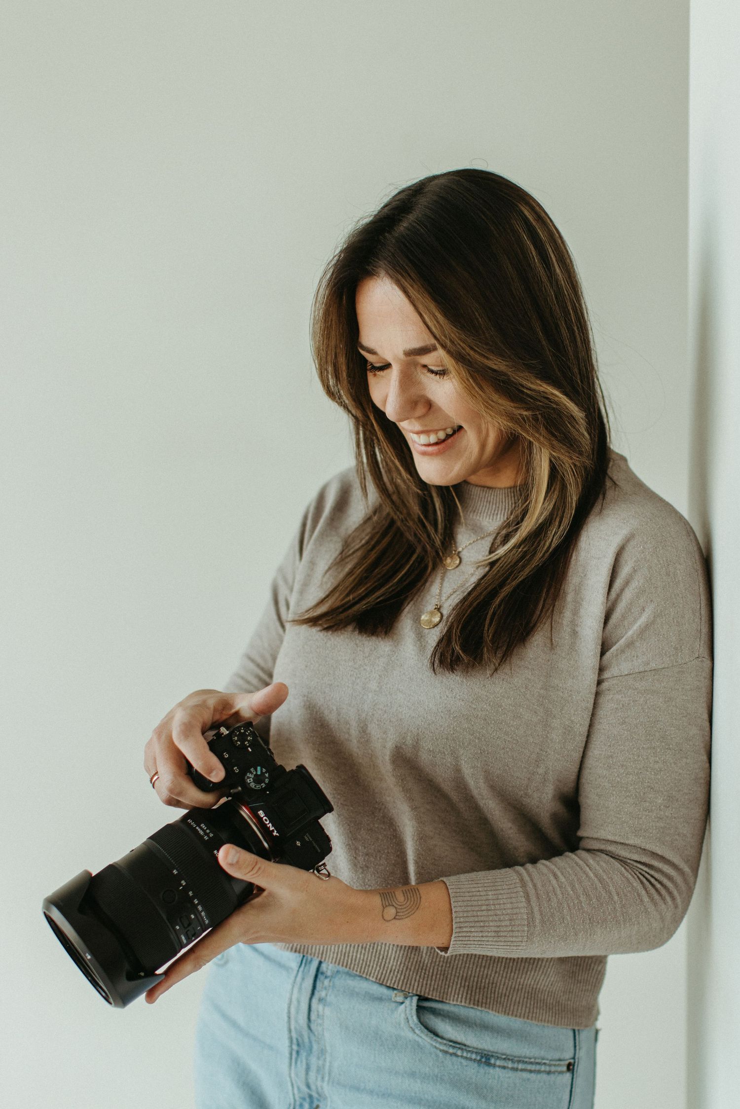Portrait of photographer holding her camera and smiling in a white studio space.