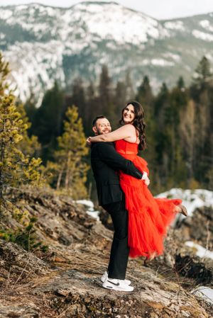 A romantic embrace captured against a backdrop of snow-capped mountains and evergreen forest.