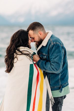Intimate moment shared between couple wrapped in striped blanket against mountain landscape.