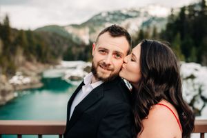 Loving couple poses on observation deck with stunning turquoise lake and mountains behind them.