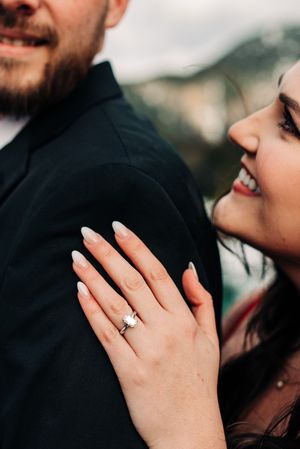 Close-up shot showing engagement ring while couple shares intimate moment against mountain backdrop.