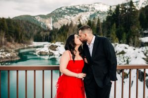 Couple in formal attire sharing romantic moment on deck overlooking turquoise mountain waters.