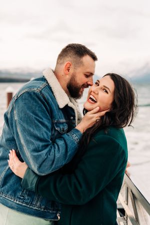A joyful moment shared between two people on a dock with mountains in the distance.