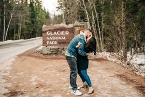A couple embraces by the Glacier National Park entrance sign in winter.
