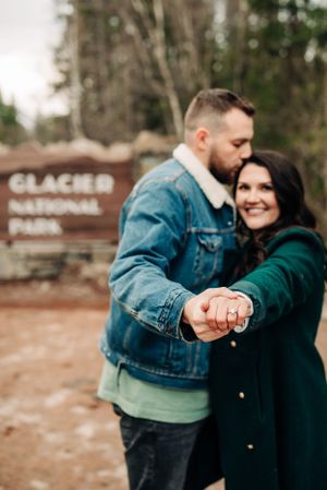 A couple shows off an engagement ring at the Glacier National Park entrance sign.