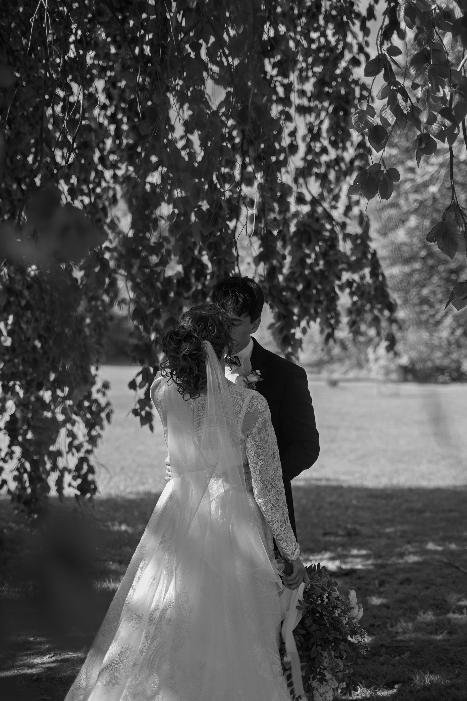 Bride and groom hold hands walking through lush green park on their wedding day.