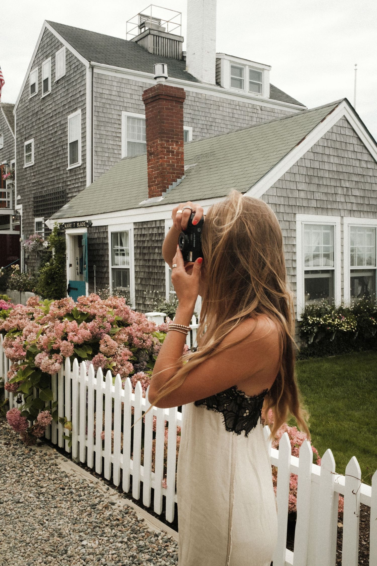 A series of photos showing someone taking pictures in front of a white picket fence with pink flowering bushes.