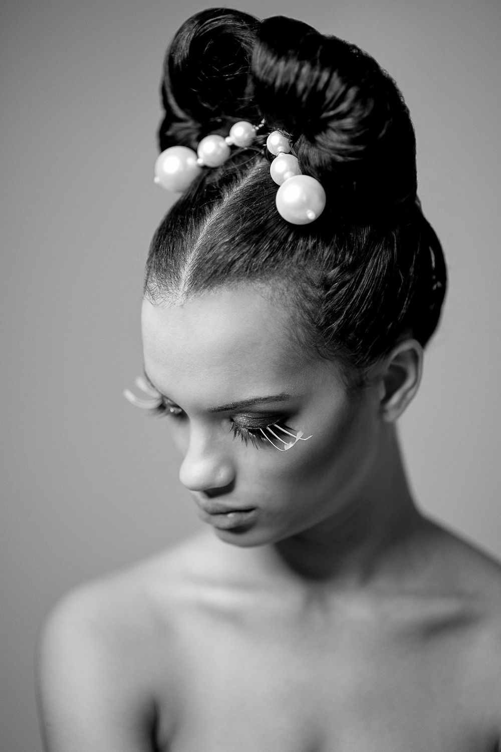 Young woman with elegant updo hairstyle adorned with pearl accessories, black and white portrait.