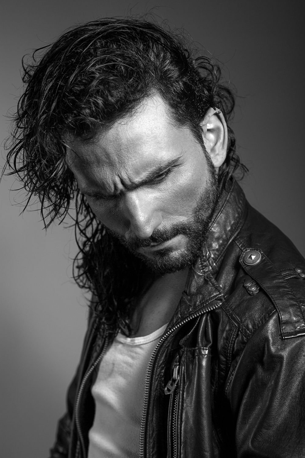 Dramatic black and white portrait of bearded man with long wet hair in leather jacket.