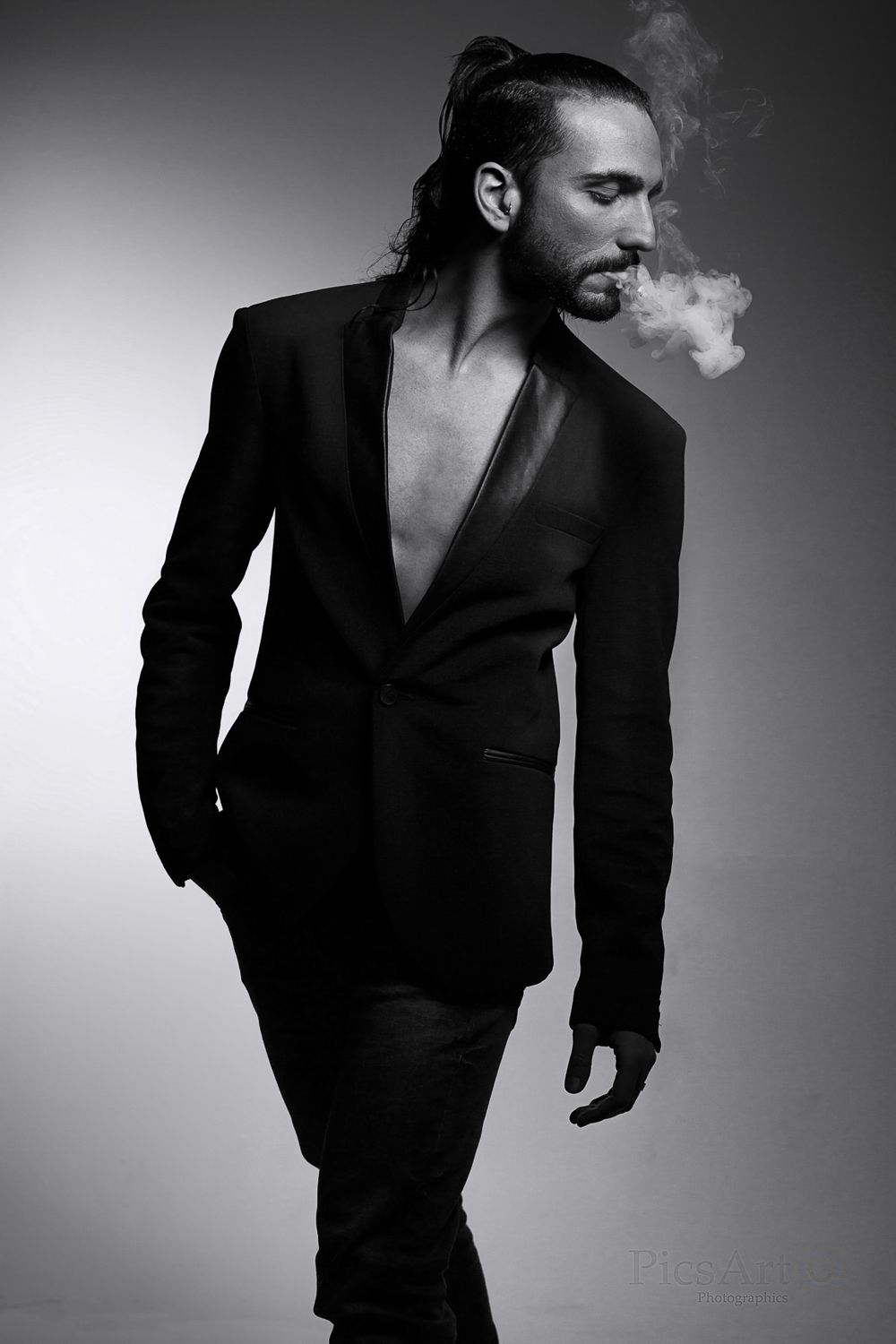 Man in black suit exhaling smoke, black and white fashion portrait.