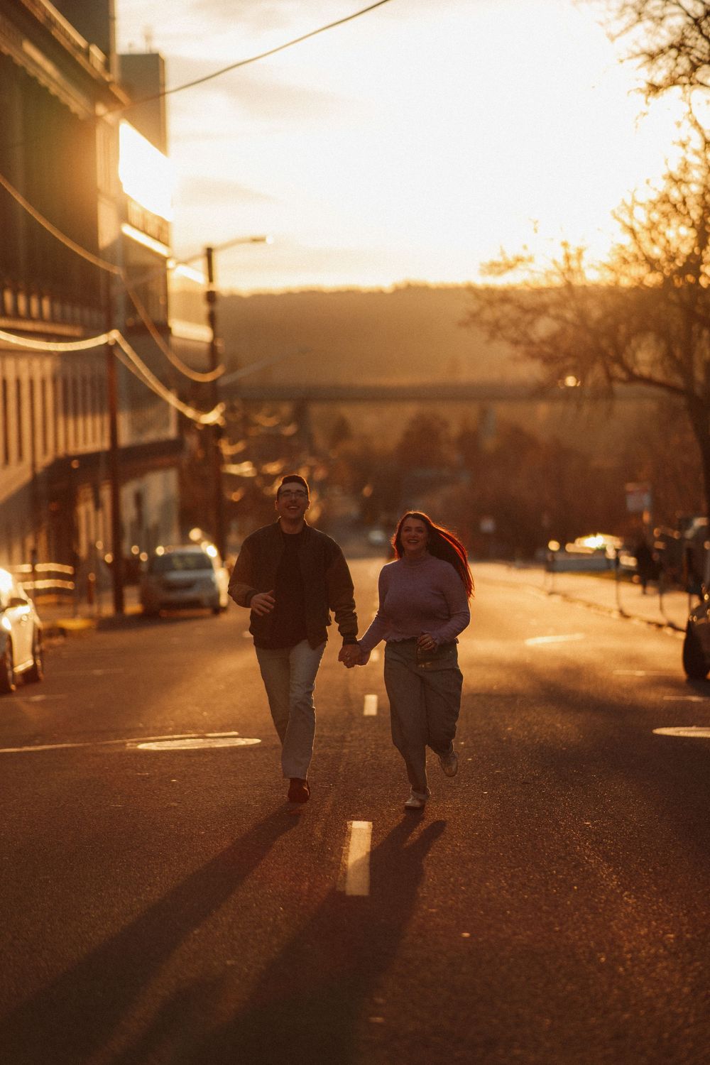 Couple holding hands running down a sunlit urban street during golden hour sunset.