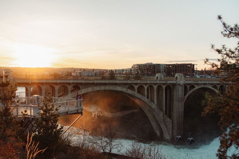 Historic stone arch bridge over a misty river at golden sunset with city buildings in the background.