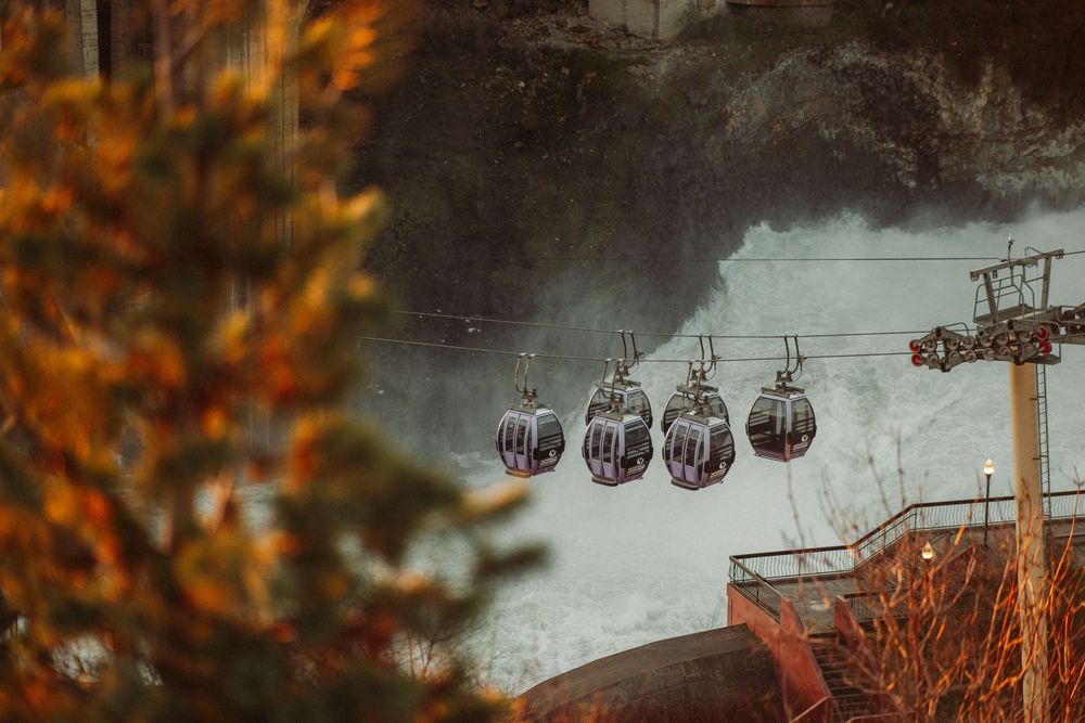 Gondola cable cars glide through misty mountain air above autumn foliage at a ski resort.