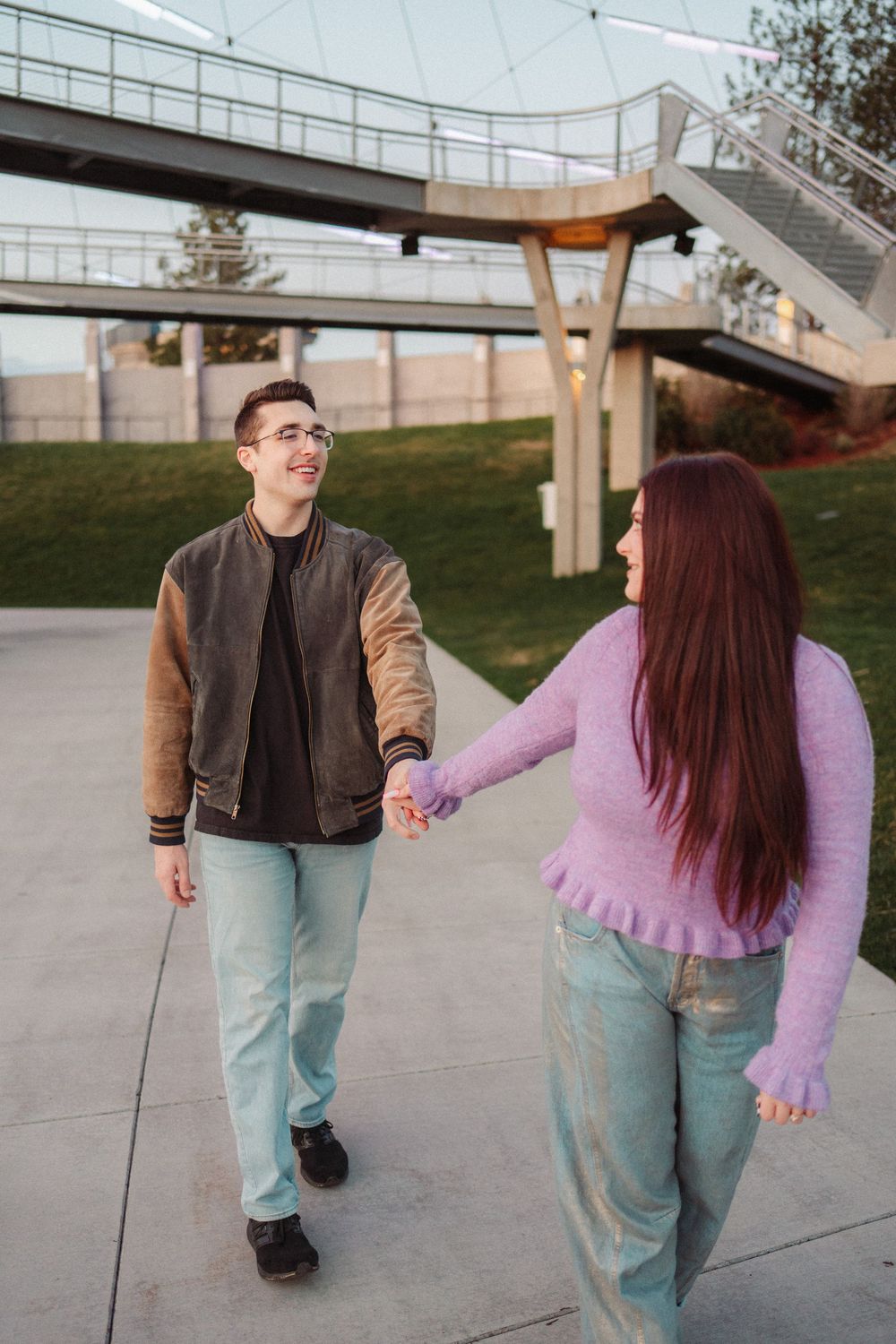 A happy couple holding hands and walking together near a modern outdoor bridge structure.