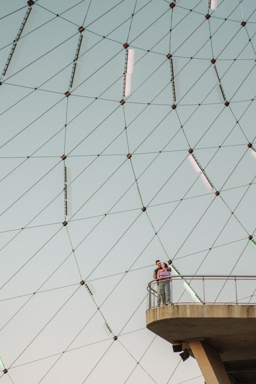 Couple standing on a scenic observation deck surrounded by a geometric cable dome structure.