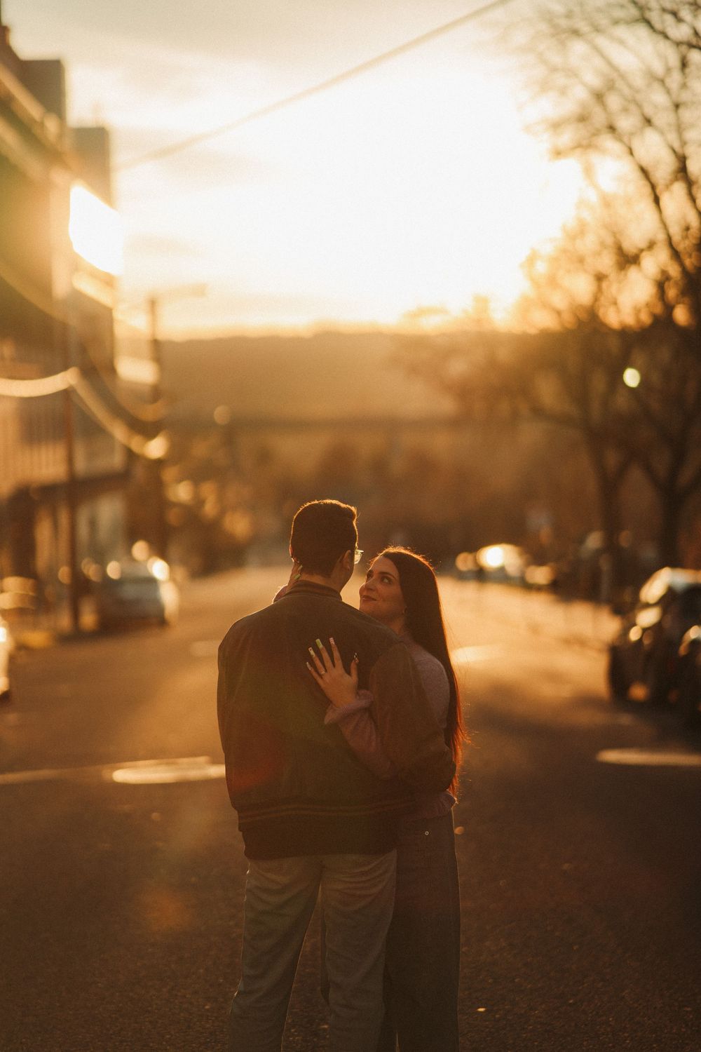 A couple embraces on a golden-lit street at sunset, surrounded by warm autumn tones.