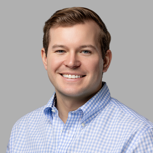 Professional headshot of a person wearing a light blue gingham button-down shirt against a neutral background.