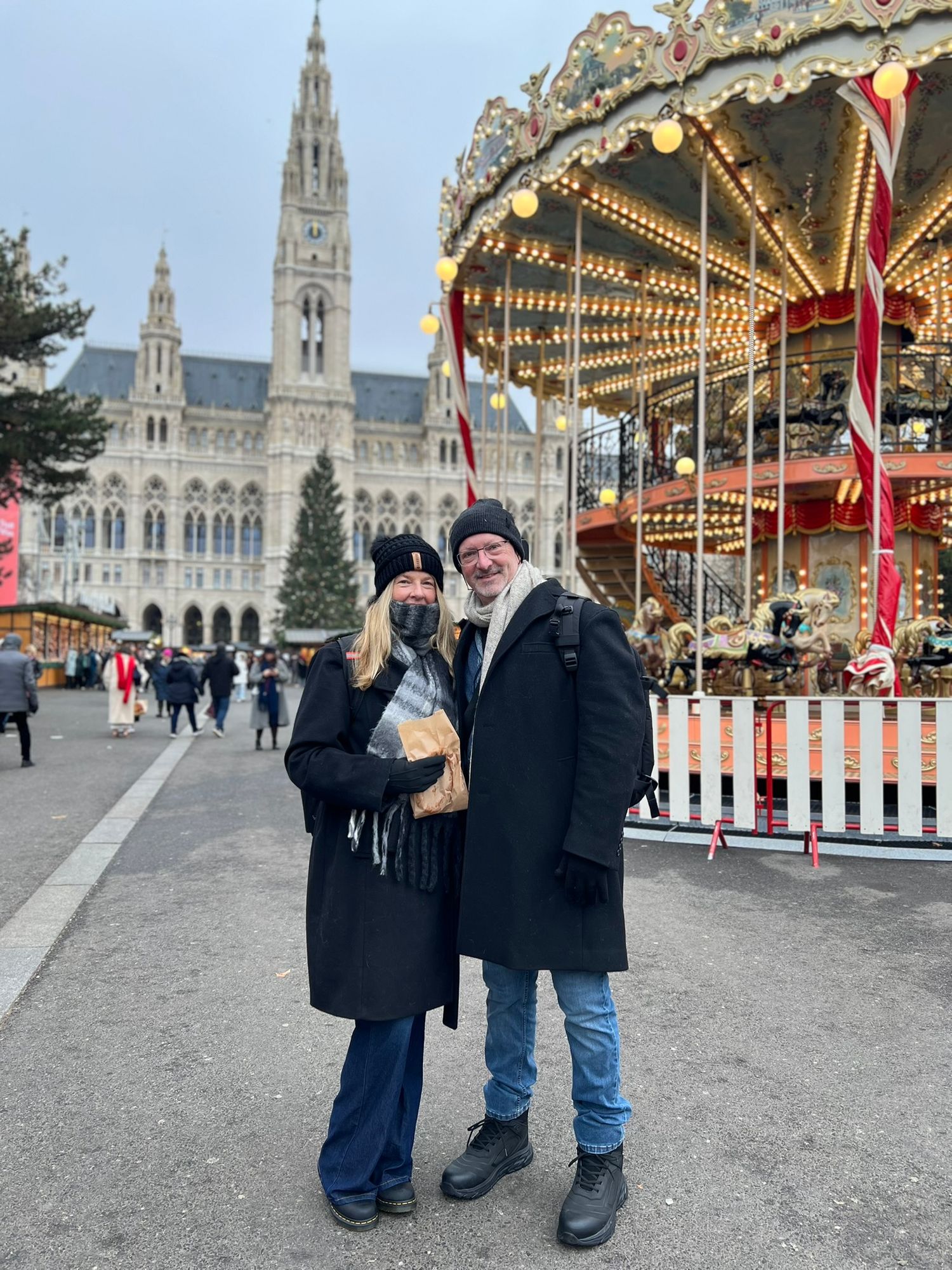 Couple posing at Vienna Christmas market with a carousel and Gothic Rathaus city hall in the background.