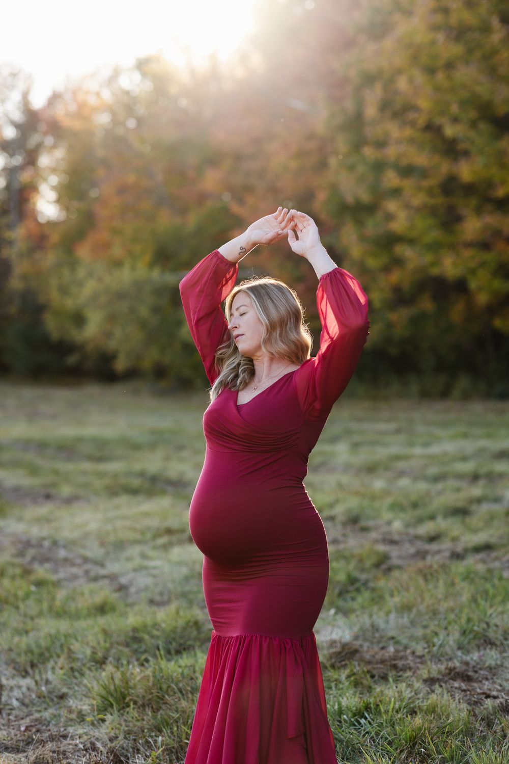 Expectant mother wears a red maternity gown in golden light with fall foliage for maternity photos. Lenox, Berkshires maternity photographer