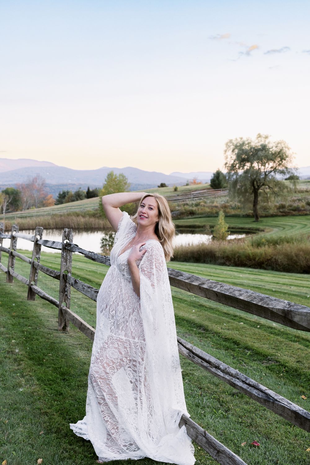 Expectant mother wears white lace dress posing in front of wooden fence for maternity photos. Lenox Berkshires maternity photographer