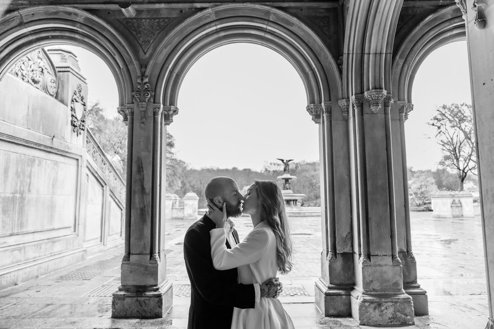 Couple sharing a romantic kiss under stone arches at Bethesda Terrace in Central Park, black and white photo.